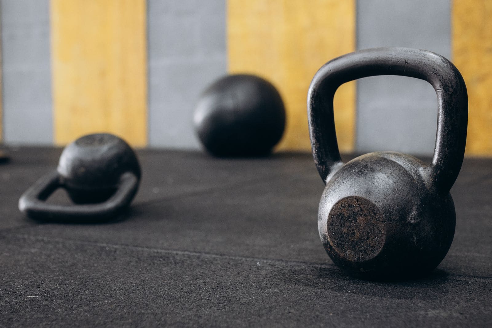 A kettlebell and medicine balls on a black gym floor